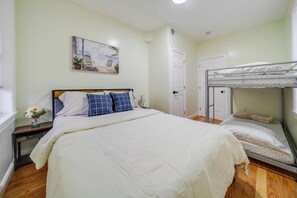 A bedroom with a single bed, a bunk bed, a nightstand, a bedside table, a wall-mounted painting, and a door.
