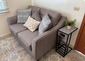 A grey sofa with patterned cushions, a small black side table with a plant, and patterned floor tiles. - Cómodo departament 5 min Garita de Otay, Aeropuerto
Zona Tranquila Wifi rapido (Tijuana)