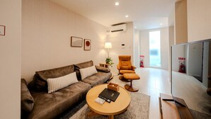 A modern living room with a brown sofa, a round coffee table, and a television. - NIKYO Sora Inn II Private Villa OSAKA (Osaka)