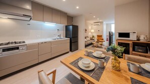 A modern kitchen with built-in appliances, a dining area with a wooden table, and a living space with a sofa and coffee table. - NIKYO Sora Inn II Private Villa OSAKA (Osaka)
