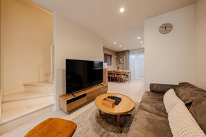 A modern living room with a flat-screen TV, a brown sofa, a wooden coffee table, and a staircase. - NIKYO Sora Inn II Private Villa OSAKA (Osaka)