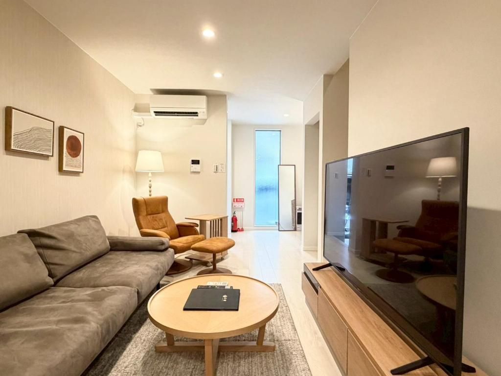 A modern living room with a sofa, armchairs, a coffee table, a TV, and artwork on the wall.