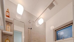 A modern bathroom with a bathtub, a shower, and a mirror. There are shelves with toiletries and a window above the bathtub. - NIKYO Sora Inn II Private Villa OSAKA (Osaka)