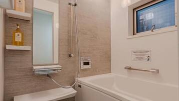 A modern bathroom with a bathtub, a shower, and a mirror. There are shelves with toiletries and a window above the bathtub.