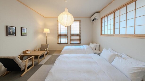 A hotel room with two beds, a desk, a chair, a lamp, and a large window with blinds. - NIKYO Sora Inn II Private Villa OSAKA (Osaka)