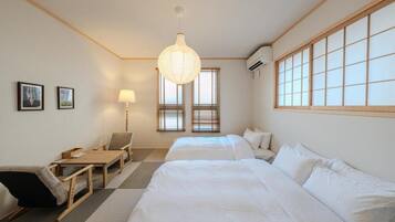 A hotel room with two beds, a desk, a chair, a lamp, and a large window with blinds.