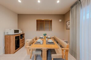 A dining area with a wooden table, chairs, and a microwave on a cabinet. - NIKYO Sora Inn II Private Villa OSAKA (Osaka)