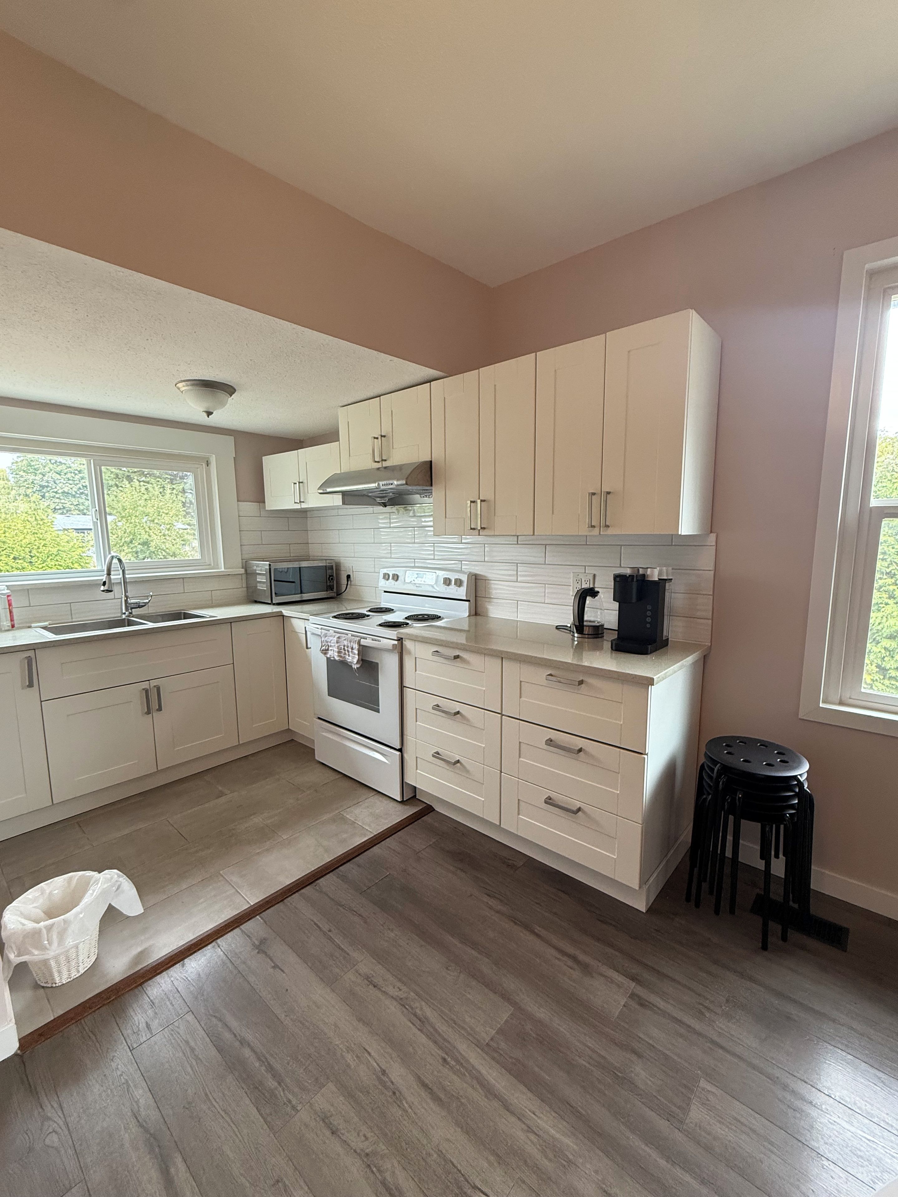 A kitchen with white cabinets, a stove, a microwave, and a window.