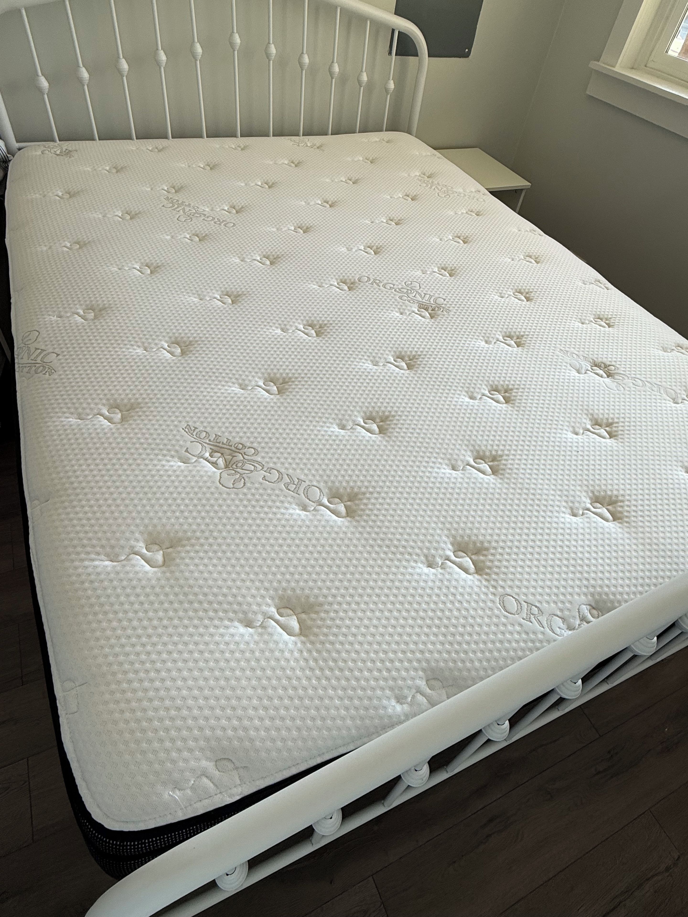 Una cama blanca con cabecera, un colchón con superficie texturizada y suelo de madera.