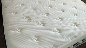 A white bed with a headboard, a mattress with a textured surface, and a wooden floor.