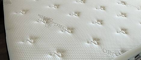Una cama blanca con cabecera, un colchón con superficie texturizada y suelo de madera.