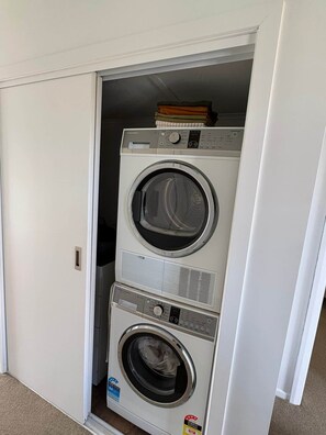 Une petite buanderie blanche, dotée de deux portes, et comprenant une machine à laver et un sèche-linge intégrés.