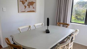 Ett matrum med ett vitt bord, sex stolar, en världskarta på väggen och ett fönster med gardiner.