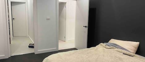 A bedroom with a bed, a dark wall, and an air conditioning unit.
