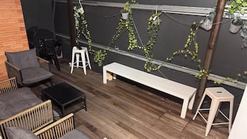 Un espace patio doté d’une terrasse en bois, de mobilier d’extérieur comprenant un banc et des chaises, et d’un mur orné de plantes grimpantes.
