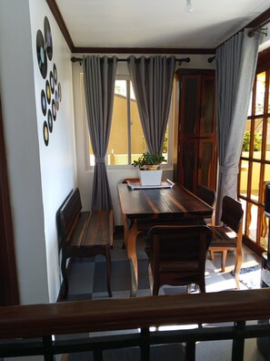 Un comedor con una mesa de madera y bancos, una planta en maceta y una ventana con cortinas.
