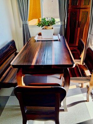 Una mesa para comer con bancos, una planta en maceta y un ventanal con cortinas.