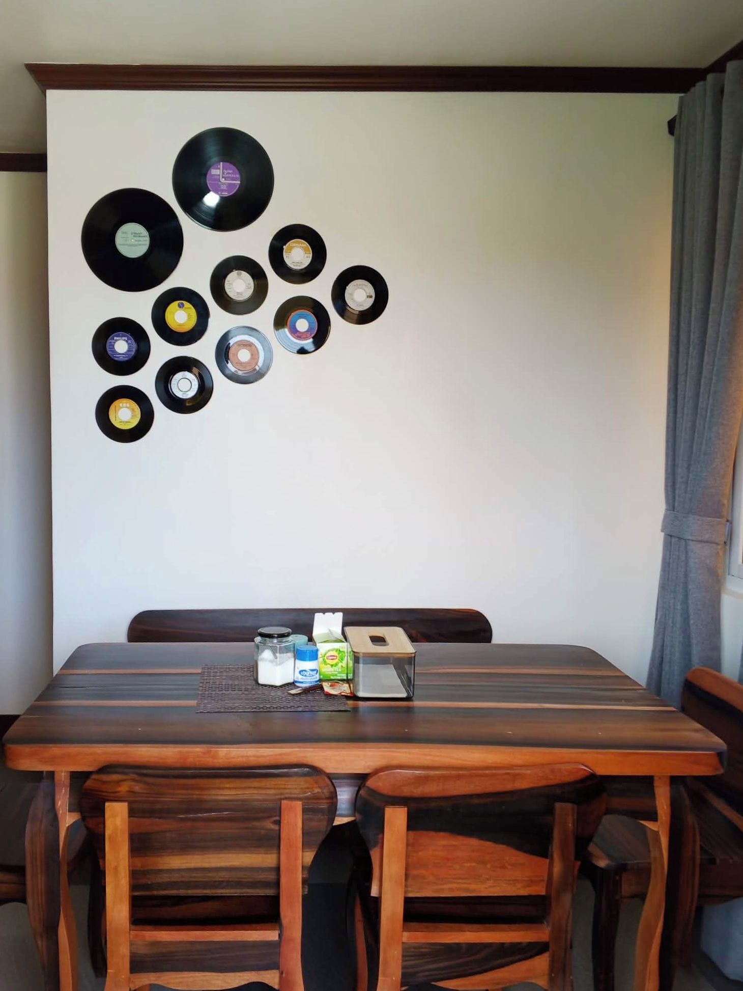 Un coin repas avec une table et des chaises en bois, un mur décoré de disques vinyles et une fenêtre avec des rideaux.