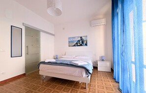 A bedroom with a bed, a nightstand, a painting, a door, and a window with curtains. - Gorgeous home in Arenella with house sea view (Arenella)