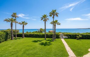 A well-maintained lawn with a pathway leading to a door, palm trees, and a clear view of the ocean. - Gorgeous home in Arenella with house sea view (Arenella)