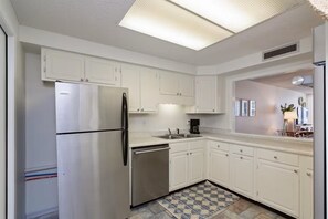 A kitchen with white cabinets, a stainless steel refrigerator, a dishwasher, and a checkered floor mat. - Ocean Front w/Direct Pvt Access, Free Beach Setup! New Owner, Pre-Reno Special! (Destin)