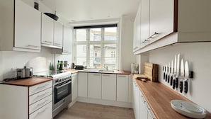 A compact kitchen with white cabinets, a built-in oven, a window with a view of buildings, and a knife block on the wall. - City Apartment in Copenhagen with 1 bedrooms sleeps 2 (Copenhagen)