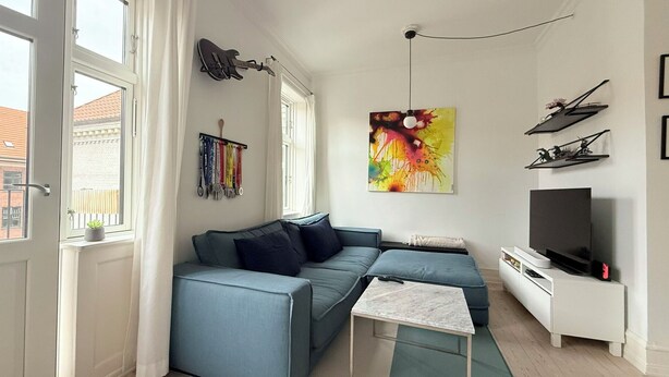 A modern living room with a sectional sofa, a small coffee table, a flat-screen TV, and a wall-mounted guitar. - City Apartment in Copenhagen with 1 bedrooms sleeps 2 (Copenhagen)