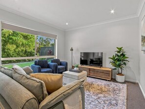 A modern living room with a sofa, chairs, a coffee table, a TV, and a plant.