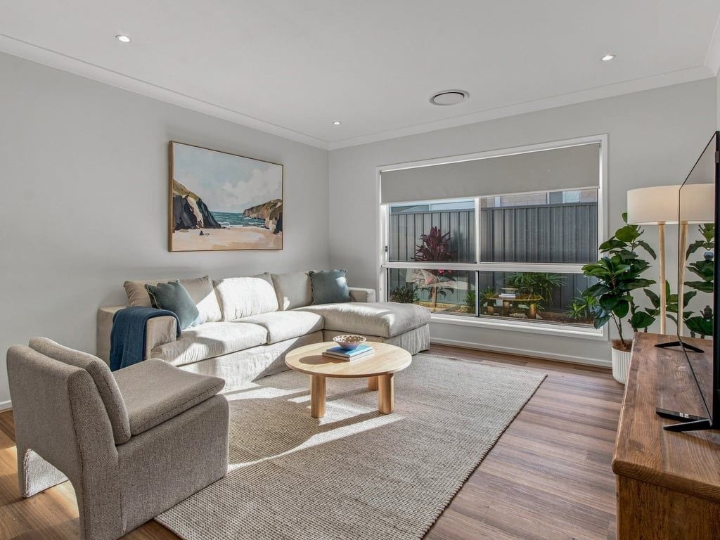 Un salon moderne avec un canapé d’angle, une table basse et une grande fenêtre donnant sur l’extérieur.