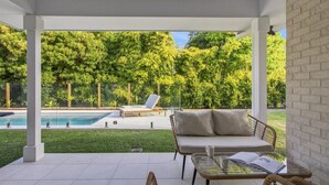 Et overdækket udendørs område med en pool, en sofa og et bord.