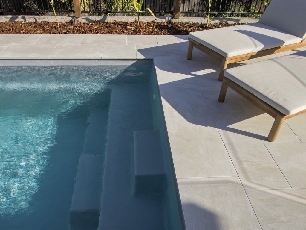 En swimmingpool med fliseterrasse og to liggestole.