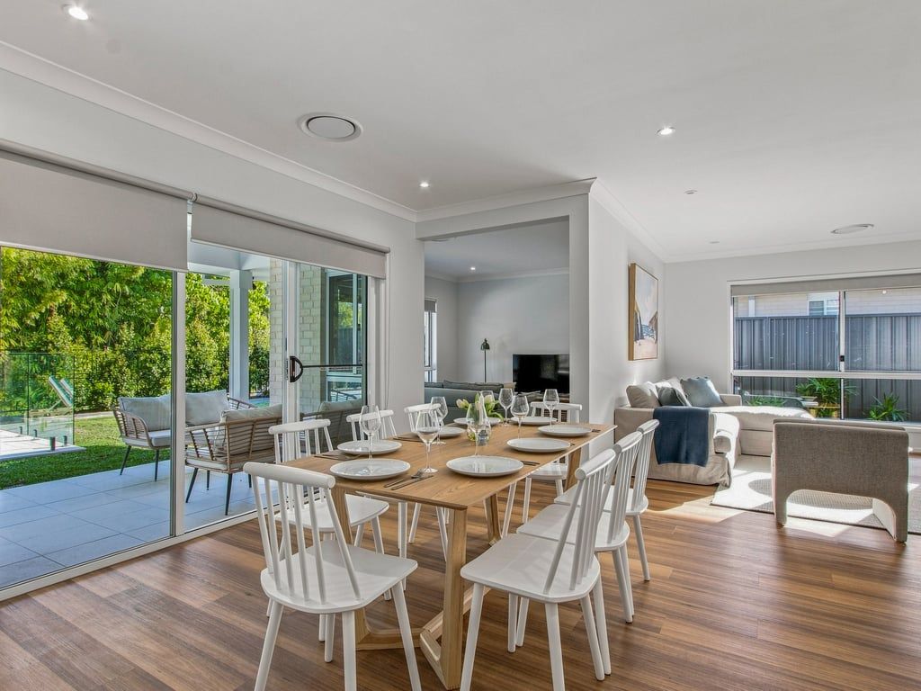 A spacious living area with a dining table, white chairs, and a sofa.