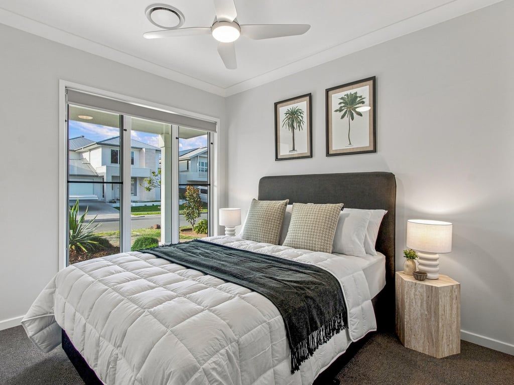 Una camera da letto con un letto, due lampade ai comodini, una ventola a soffitto e vista su un quartiere residenziale tramite una porta scorrevole.