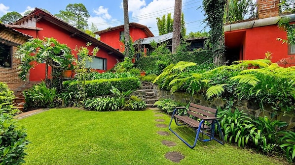 A red brick house with a well-maintained garden, a wooden bench, and a stone staircase leading to the entrance.