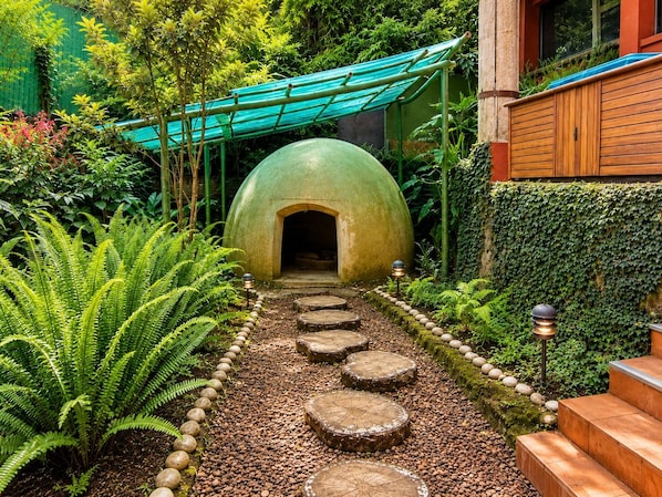A garden pathway leading to a green dome structure, surrounded by lush greenery and stone steps.