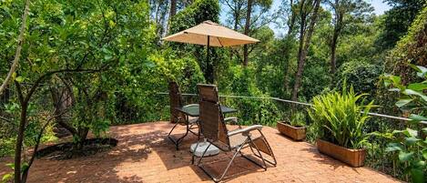 Eine Terrasse im Freien mit Tisch und Stühlen, umgeben von Grünpflanzen und Bäumen.