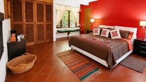 A bedroom with a large bed, a nightstand, a lamp, a window with curtains, a wooden wardrobe, and a wicker basket. - Quetzal Suite | Terrace, fireplace and jacuzzi (Valle de Bravo)