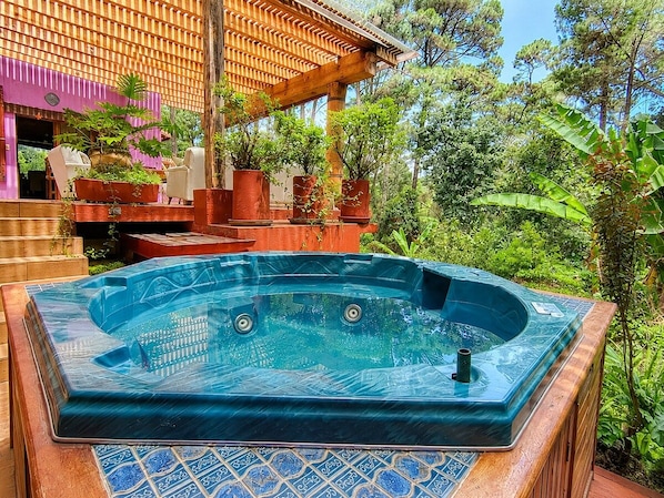 Un bain à remous installé dans un jardin, avec une terrasse en bois et des plantes en pot.