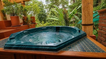 Un bain à remous installé à l’extérieur, accessible par des marches, entouré de verdure et bordé d’un mur en briques.