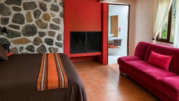Une chambre à coucher avec un lit, un canapé rouge, un mur en pierre et un téléviseur.