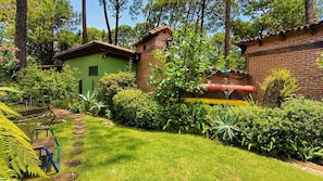 A green house with a brick chimney, surrounded by a well-maintained garden with a variety of plants and a wooden bench.