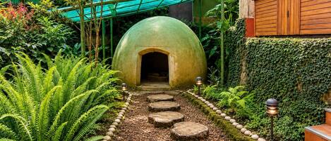Un sentier de jardin mène à une structure en forme de dôme verdoyant, entourée d’une végétation luxuriante et de marches en pierre.