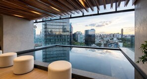 En modern takterrass med en glasräcke, utsikt över stadens silhuett och minimalistisk sittgrupp.