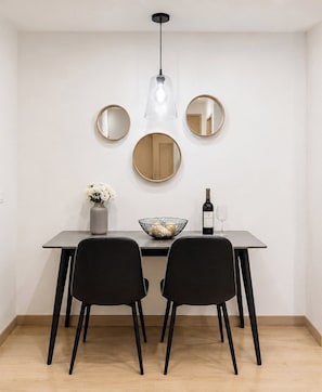 A dining area with a table, chairs, a vase of flowers, a wine bottle, and three mirrors on the wall. - Premium Loft Reforma | View + Pool + Gym (Mexico City)