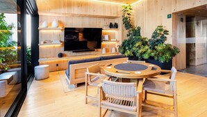 A modern interior with a round wooden table, cushioned seating, a flat-screen TV, and a large potted plant. - Premium Loft Reforma | View + Pool + Gym (Mexico City)