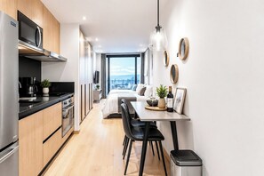 A modern kitchen with a built-in microwave, stove, and oven. There is a dining area with a table and chairs, and a bed with a city view. - Premium Loft Reforma | View + Pool + Gym (Mexico City)