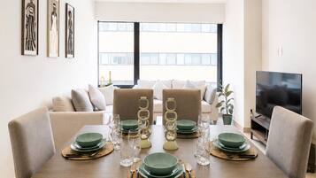 A dining area with a wooden table set for four, surrounded by sofas and a television.