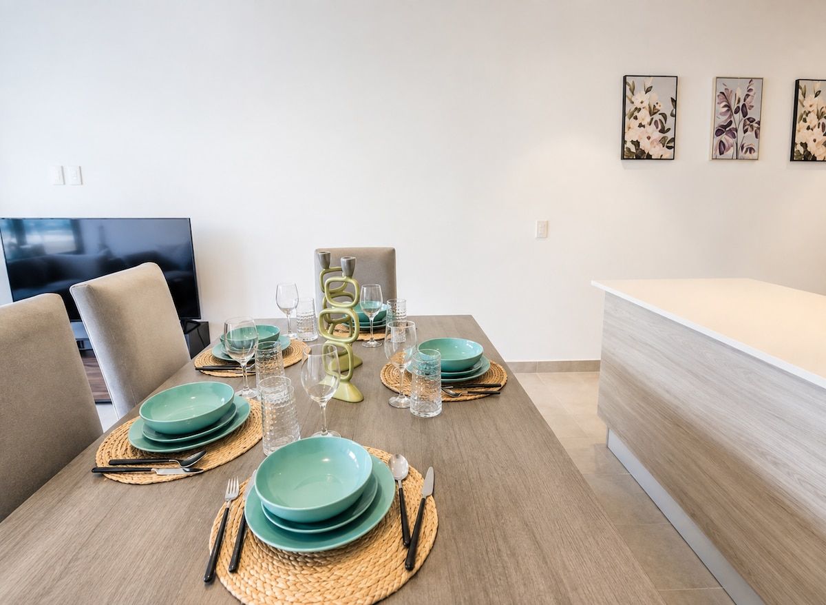 Un comedor con una mesa dispuesta para cuatro personas, incluyendo platos, vasos y cubiertos.