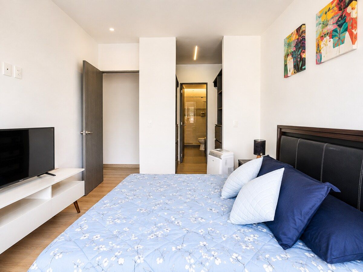 A modern bedroom with a bed, a television, and a bathroom visible through an open door.
