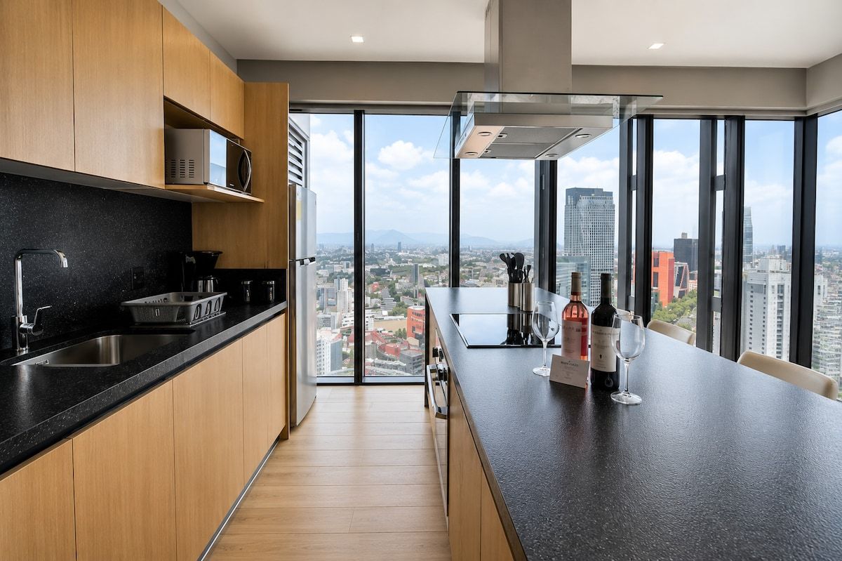 A modern kitchen with a large window, a microwave, and a wine bottle on the counter.